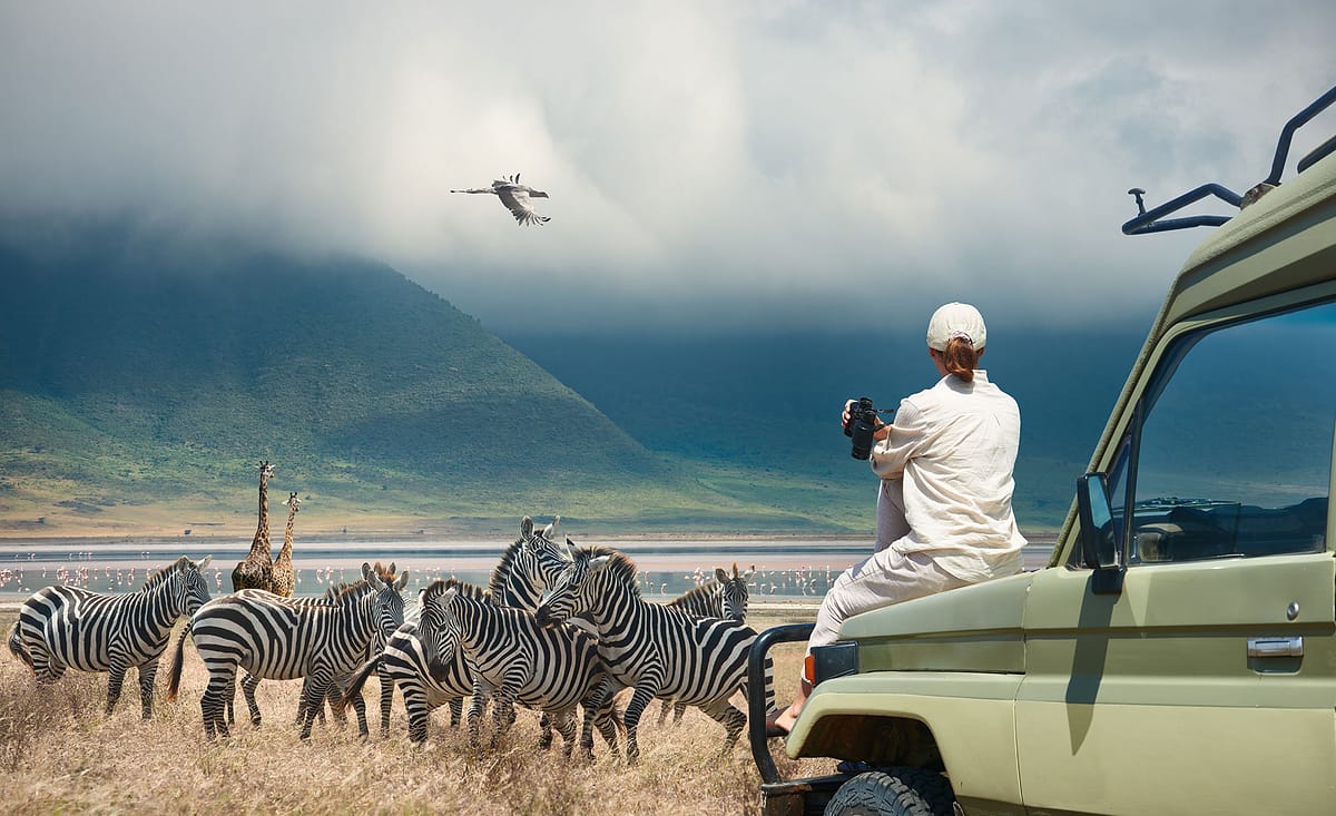 A woman sits on the hood of her safari vehicle wearing appropriate safari clothes