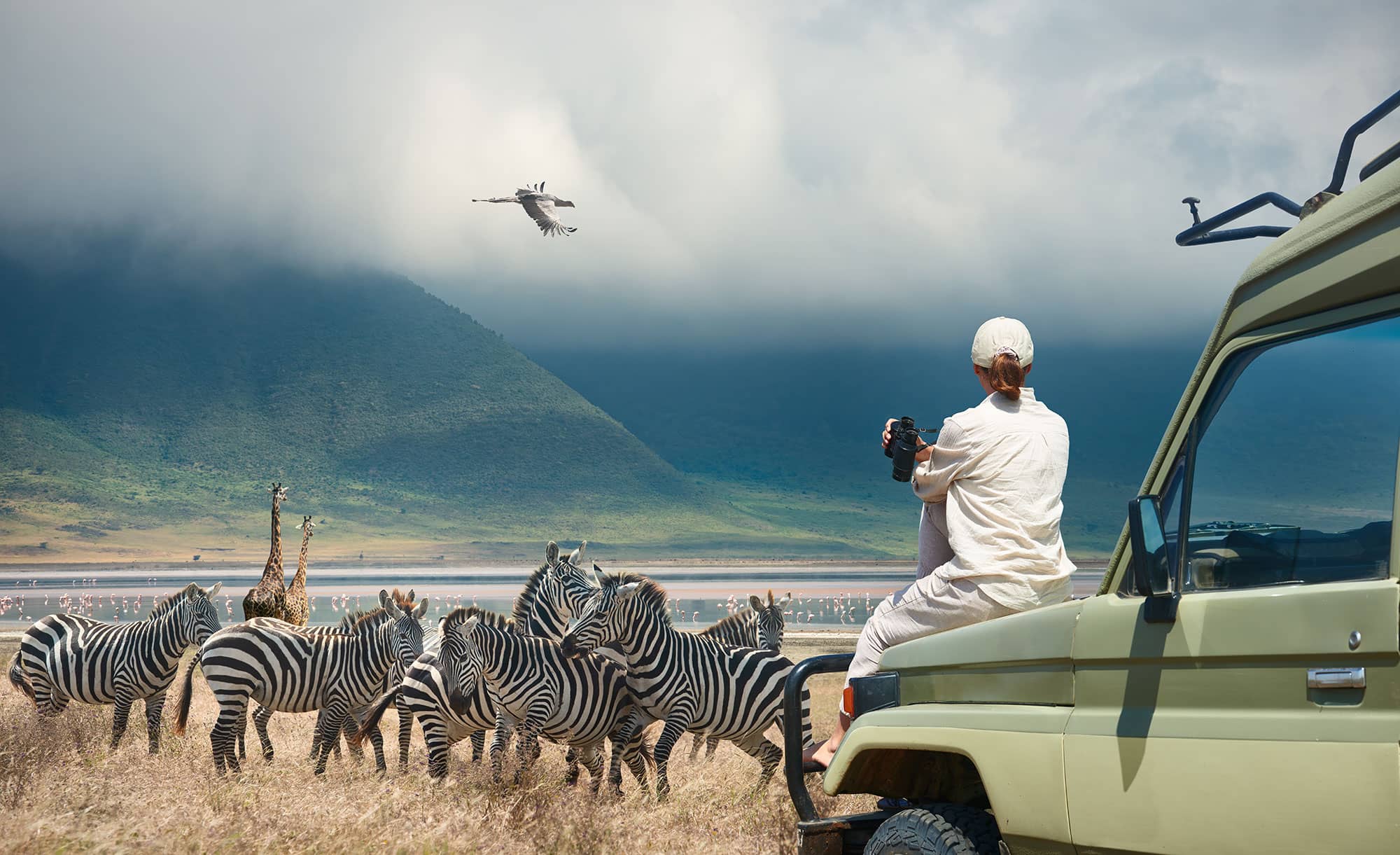 A woman sits on the hood of her safari vehicle wearing appropriate safari clothes