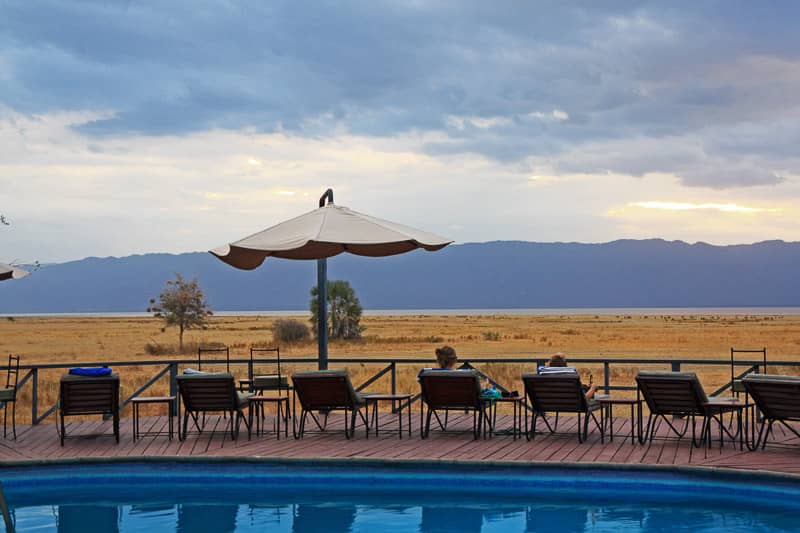 Two people relax by a pool but instead look out over the Tanzanian landscape behind them.